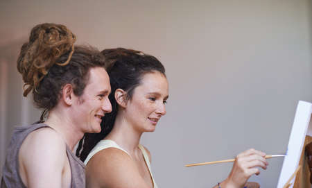 Adding a touch of her own unique style. A cropped view of a young artist painting with her boyfriends support.の写真素材