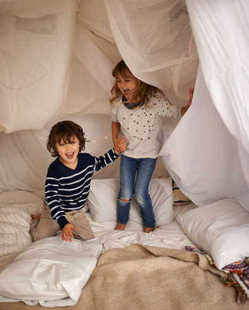 The best memories are made with my brother. Shot of two adorable siblings jumping on the mattress underneath their fort.の写真素材