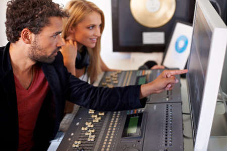 Enjoying the advantages of digital recording technology. A young audio engineer pointing at a...