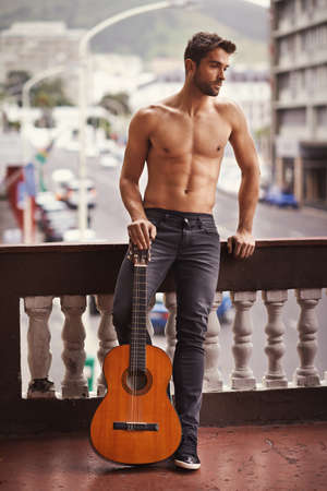 Finding peace in the noise. Cropped shot of a shirtless young man with his guitar.の写真素材