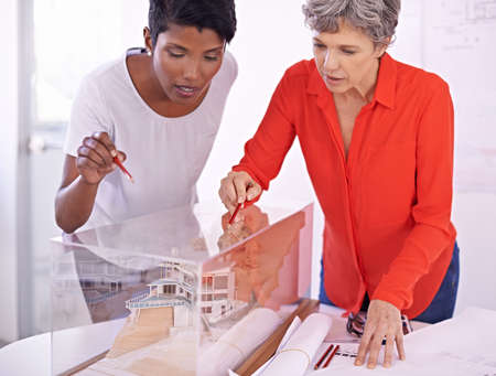 Two heads are better than one. Shot of two female architects discussing an architectural model.の写真素材