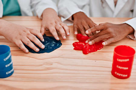 Were getting stuck in the fun of it all. Cropped shot of two unrecognizable school pupils playing and experimenting with slime in science class at school.の写真素材