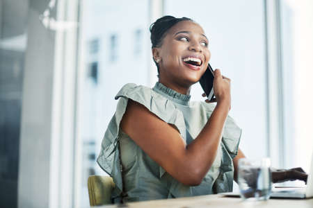 Working on that client rapport. Shot of an attractive young businesswoman sitting in the office and using her laptop while talking on her cellphone.の写真素材