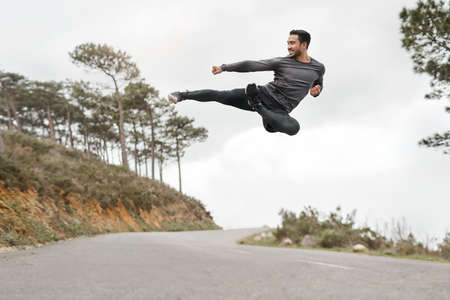 My body is built to overcome obstacles. Full length shot of a handsome young man doing a flying kick during his workout outdoors.の写真素材