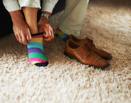 Adding a little bit of fun to the outfit. Cropped shot of a man putting on colourful socks and loafers.の写真素材