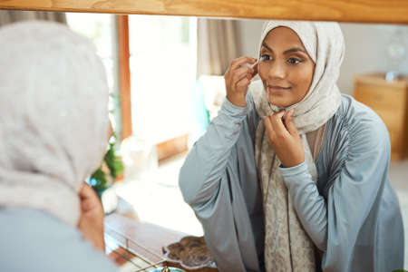 Ready to hit the road. Shot of a young muslim woman using the mirror at home.の写真素材