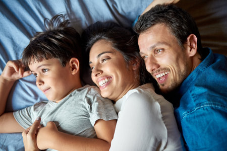 Woke up surrounded by love. Shot of a beautiful young couple and their son laying in bed together at home.の写真素材