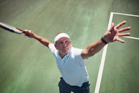 Ready, set, go. High angle shot of a handsome mature sportsman playing tennis alone on a court during the day.の写真素材