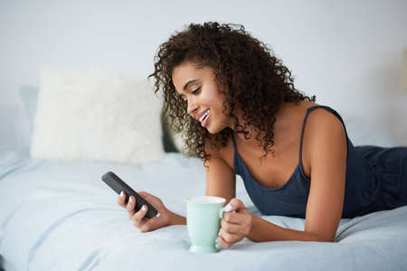 The morning routine of checking social media. Shot of an attractive young woman lying on her bed and...