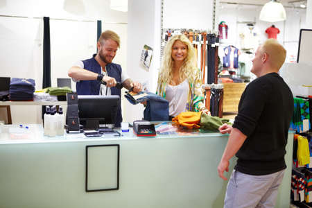 Fast and friendly point of sale. Two sales clerks helping a customer purchase a pair of jeans in a clothing store.の写真素材