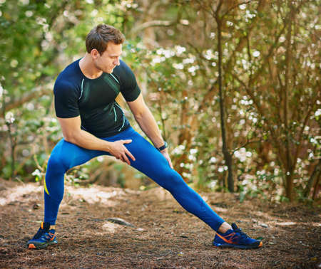 Stretch and stretch some more. Shot of a young man stretching before a trail run.