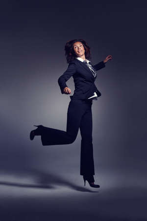 Taking everything in her stride. A businesswoman jumping against a dark background.の写真素材