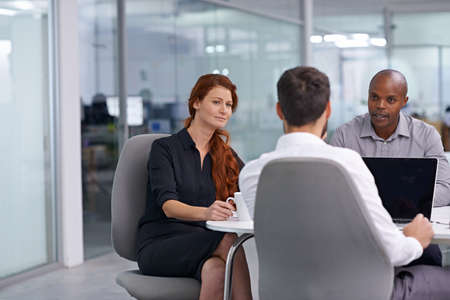 Putting him on the spot. A group of coworkers having a meeting in an office.