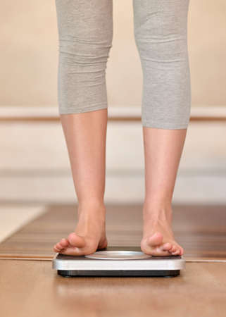 Those digits are finally decreasing. Closeup shot of a young woman weighing herself on a scale at home.の写真素材