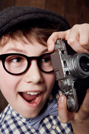 What a great shot. Young boy in retro clothing wearing spectacles and holding up his camera.
