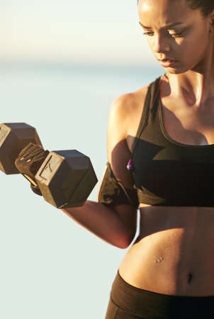 Building her biceps. Shot of a young woman exercising outdoors.の写真素材