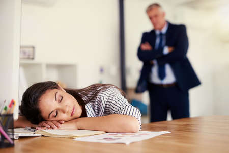 Shes been caught sleeping on the job. Cropped shot of a businesswoman sleeping at her desk with her boss standing in the background.の写真素材
