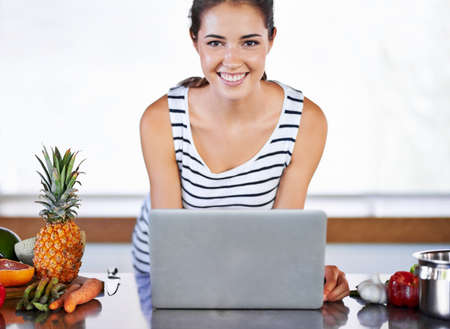 The internet makes cooking SO easy. A beautiful young woman browsing the internet for recipes in her kiitchen.の写真素材