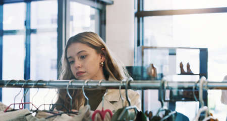 Its always a good idea to go shopping. Shot of a young woman browsing through clothes in a boutique.の写真素材