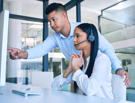 Take charge and make a change. Shot of a young man helping his colleague in a modern call centre.の写真素材