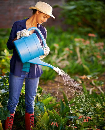 Make it rain. Shot of a young woman watering her garden.