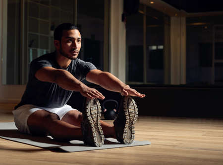Warming up before the workout. Full length shot of a handsome young male athlete going through his warmup routine in the gym.の写真素材