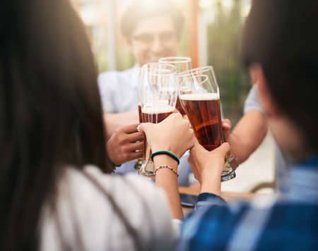 Whos buying the second round. Shot of a group of cheerful young business colleagues having a celebratory toast with beer around a table outside.の写真素材