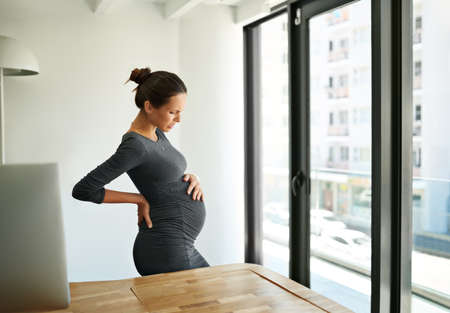 Any day now.... Shot of a pregnant businesswoman standing in her office holding her stomach.