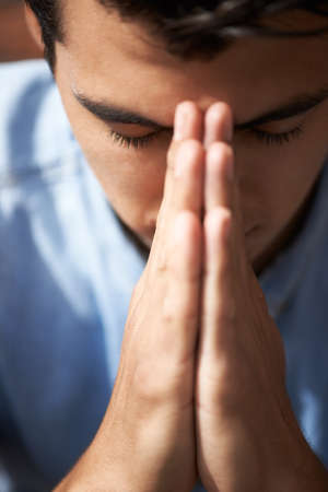 Hoping and praying. Closeup of a young man praying with his hands together.の写真素材