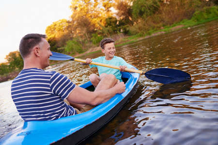 Row row row your boat. Shot of a father and son rowing a boat together on a lake.の写真素材