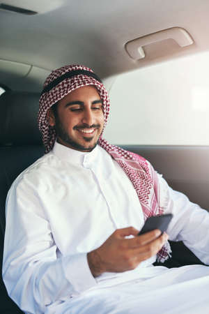 En route to success. Shot of a young muslim businessman using his phone while traveling in a car.の写真素材