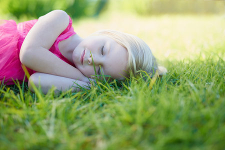 Catching a snooze in the sun. Cropped shot of a cute little girl sleeping on the grass outside.の写真素材