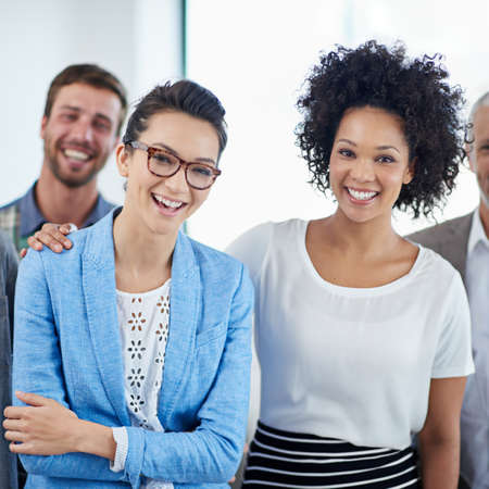 Teamwork with a smile. Portrait of two female coworkers smiling in an office with colleagues in the...