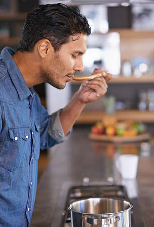 My moms recipes are always the best. Shot of a handsome man tasting food while heamp039s cooking at...