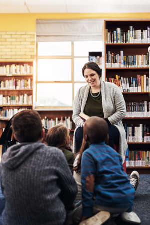 Shes sharing her love for books to the class. Shot of a teacher reading to a group of elementary...