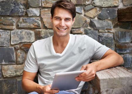 Portrait of a young man smiling at the camera while holding his digital tablet outdoorsCropped shot of a man using his digital tablet while sitting on the deckの写真素材