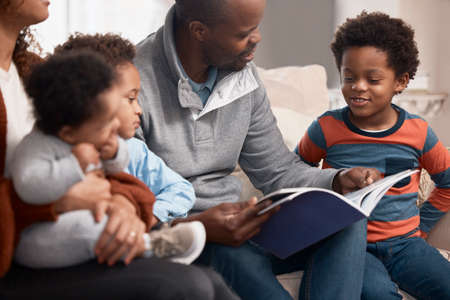 Its become a tradition in their family to read together. Shot of a father reading a book to his family at home.の写真素材