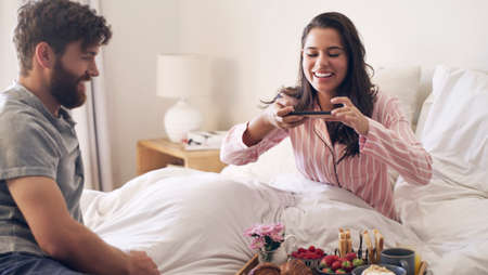 This is why I married him. Shot of a young woman taking a picture of the breakfast her husband has...