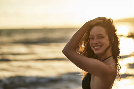 Shes a breezy beach beauty. Portrait of a happy young woman posing on the beach at sunset.の写真素材