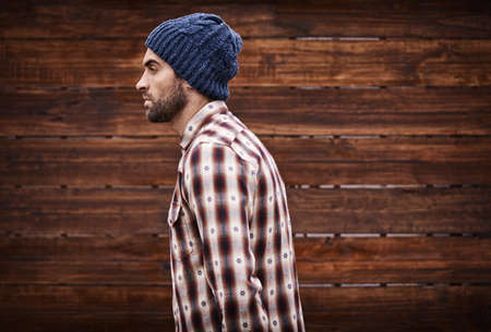 Styled for the street. Shot of a handsome young man in trendy winter attire against a wooden background.の写真素材