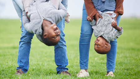 Do anything, but let it produce joy. Shot of two children hanging upside down by their parents outside.の写真素材