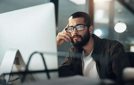 The later it gets the deeper he goes. Shot of a young businessman using a computer during a late...