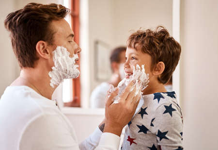 Now is a good time for his first shaving lesson. Shot of a man teaching his young son how to shave at home.の写真素材