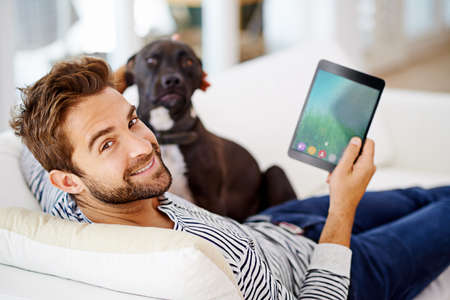 Its one of those hanging-out-on-the-couch days. Man using his tablet on his couch.