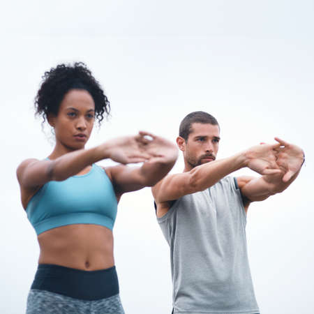 Loosening their joints before their run. Shot of two sporty young people stretching while exercising outdoors.の写真素材