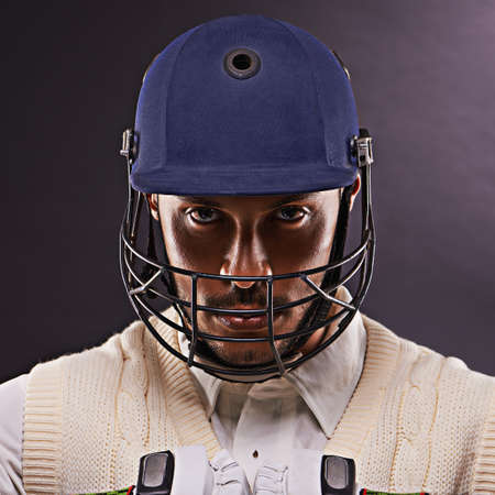 Confident in his batting ability. A cropped shot of an ethnic young man in cricket attire isolated on black.の写真素材