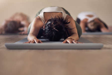 Yoga is our way of life. Shot of a group of unrecognizable people meditating and working out together in a yoga class.の写真素材