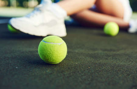 Grab a racket and ball and get playing. Closeup shot of a tennis ball on a tennis court with an unrecognisable woman sitting in the background.の写真素材