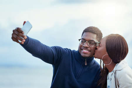 Theyre definitely madly in love. Shot of an affectionate young couple taking selfies together outdoors.の写真素材