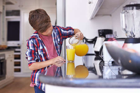 Mom said I could help myslef. A young boy drinking a glass of orange juice.の写真素材